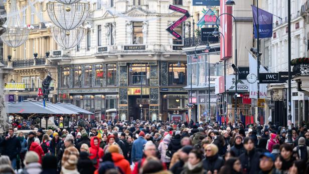 Viele Menschen gehen dicht gedrängt durch eine belebte Einkaufsstraße mit historischen Gebäuden und zahlreichen Geschäften.
