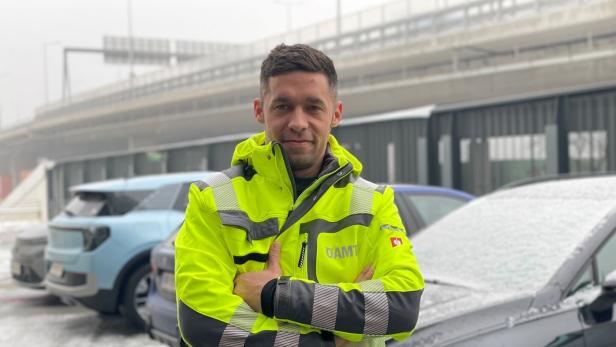 Der Pannenfahrer mit gelber Warnjacke des ÖAMTC vor verschneiten Autos.