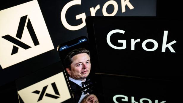 Ein Mann ist auf einem Smartphone-Bildschirm zwischen den Schriftzügen „Grok“ und einem stilisierten X-Logo zu sehen.