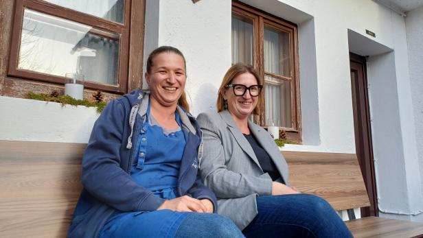 Die Almwirtinnen Agi und Michi sitzen auf einer Bank vor ihrem Gasthaus. 
