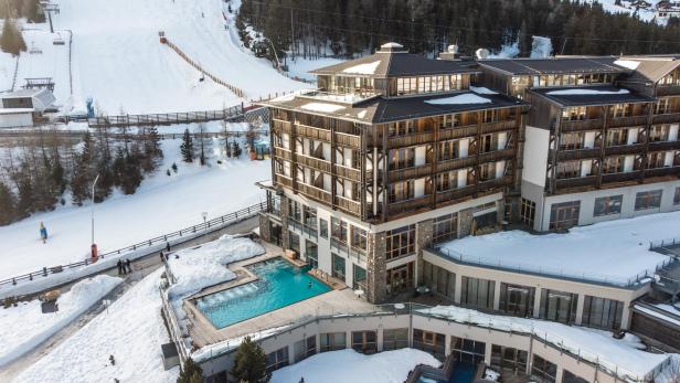 Hotel mit Außenpool direkt an einer verschneiten Skipiste in alpiner Winterlandschaft.