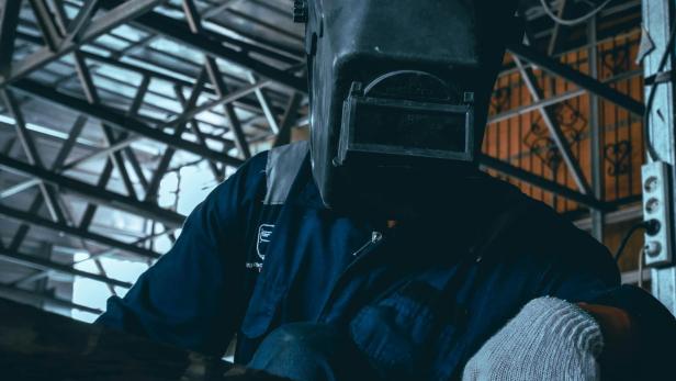 Ein Arbeiter mit Schutzmaske und Handschuhen arbeitet in einer industriellen Produktionshalle.