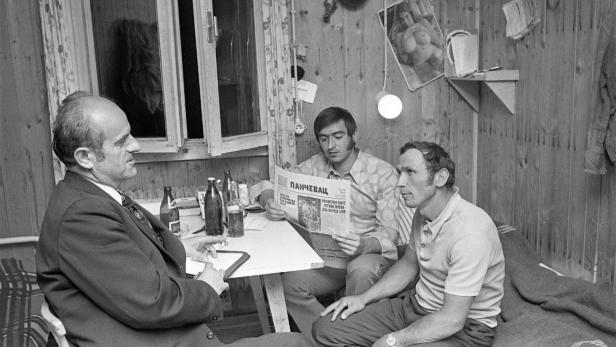 Drei Männer sitzen um einen Tisch in einer Arbeiterunterkunft.