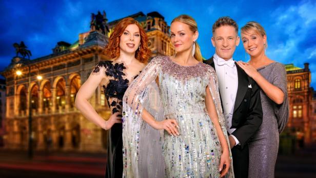 Vier elegant gekleidete Personen posieren vor einem beleuchteten historischen Gebäude am Abend.