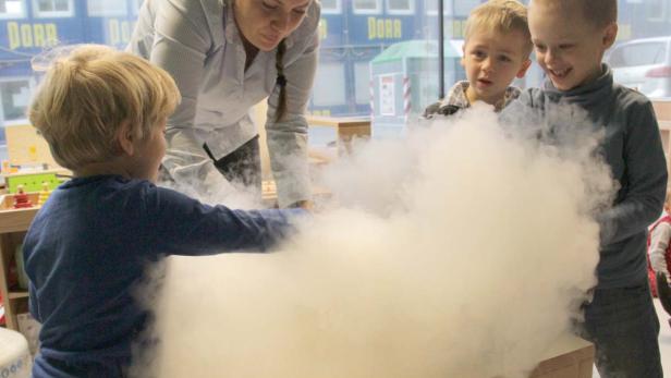 Kinder und eine Frau beobachten dichten Nebel in einem Innenraum.