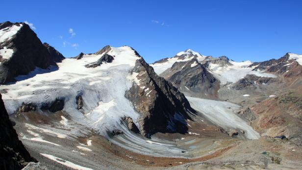 Eine Berglandschaft mit schneebedeckten Gipfeln und einem Gletscher unter blauem Himmel.