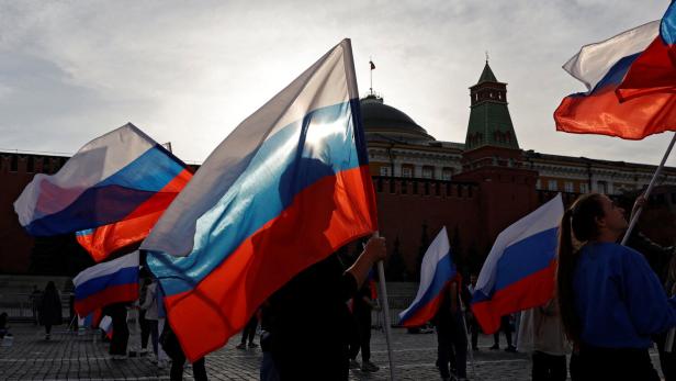 Menschen halten russische Flaggen vor dem Hintergrund des Moskauer Kremls.