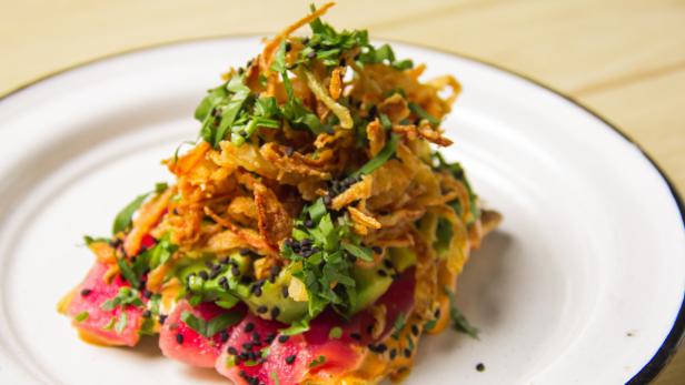 Auf einem Teller liegt ein Gericht mit Thunfisch, Avocado, frittierten Zwiebeln und Kräutern.