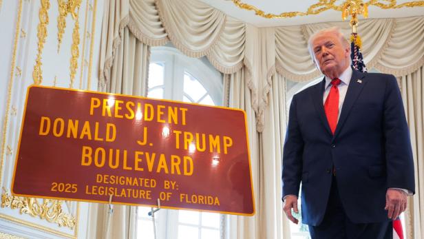 Donald Trump steht neben einem Schild mit der Aufschrift "President Donald J. Trump Boulevard".