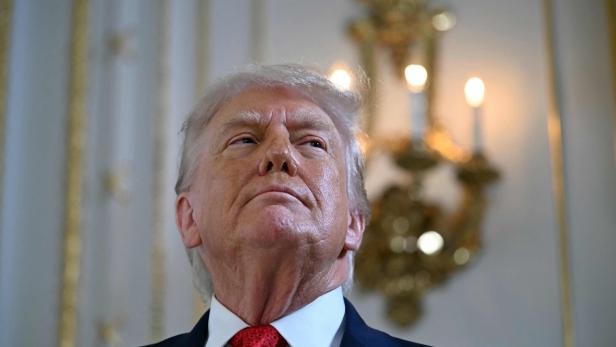 Donald Trump blickt mit roter Krawatte und Anstecknadel der US-Flagge nach oben.