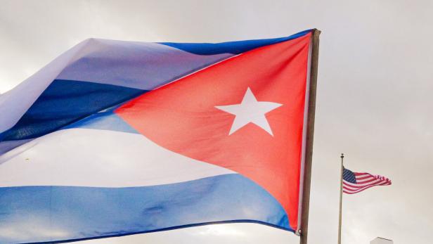 Eine kubanische Flagge weht im Wind, im Hintergrund ist eine amerikanische Flagge zu sehen.