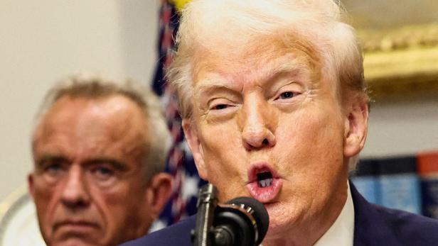 Donald Trump spricht am Mikrofon, eine weitere Person ist im Hintergrund zu sehen.