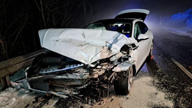 Stark beschädigtes weißes Auto nach Frontalzusammenstoß auf winterlicher Landstraße.