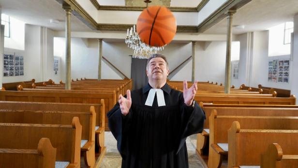 Ein Pfarrer jongliert in einer Kirche mit einem Basketball.