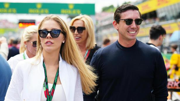 Eine blonde Frau mit Sonnenbrille und Akkreditierung geht neben einem lächelnden Mann.