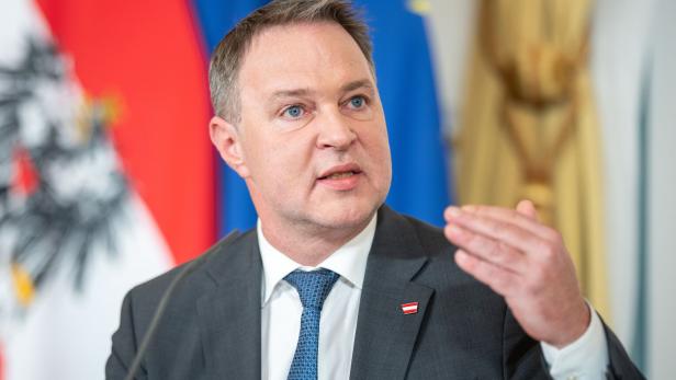 Andreas Babler im Anzug vor den Flaggen Österreichs und der EU.