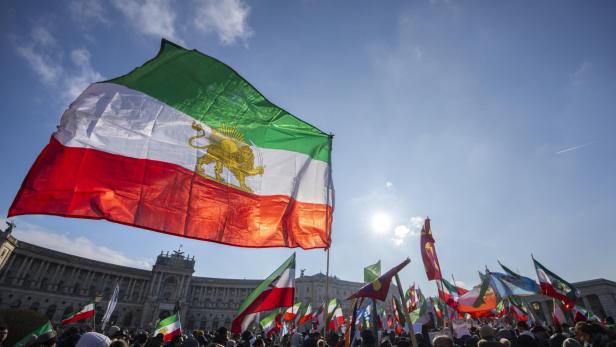 Viele Menschen versammeln sich mit zahlreichen Fahnen, darunter eine große Flagge mit Löwen- und Sonnensymbol.