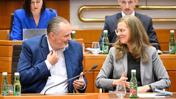 Zwei Personen im Anzug unterhalten sich freundlich an einem Konferenztisch, im Hintergrund sitzen weitere Menschen.