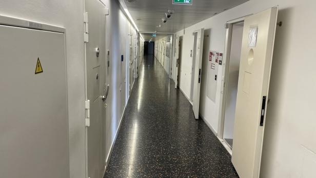 Ein langer Flur mit weißen Türen und einem Notausgangsschild erstreckt sich in die Ferne.