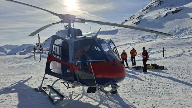 Ein Rettungshubschrauber steht im Schnee, während Einsatzkräfte in orangefarbener Kleidung daneben stehen.
