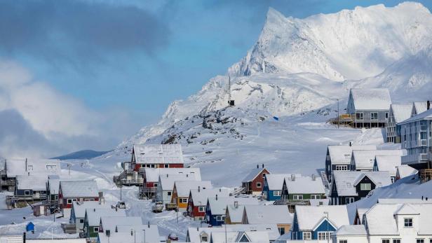 Schneebedecktes Dorf mit bunten Häusern vor einer hohen, verschneiten Bergkulisse.