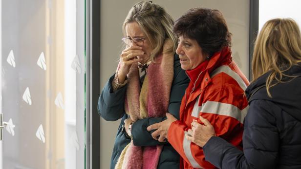 Eine weinende Frau mit Brille wird von einer Frau in roter Jacke getröstet.