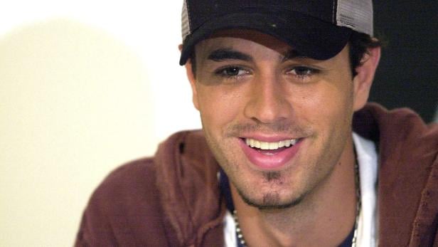 Ein lächelnder Enrique Iglesias mit Kappe und braunem Hoodie blickt zur Seite.