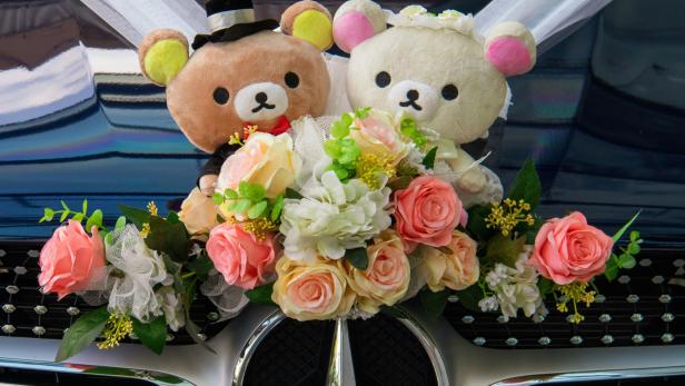 Zwei Plüschbären als Brautpaar mit Blumenstrauß sind an einem Autogrill befestigt.