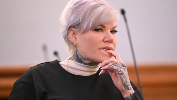 Melanie Müller mit kurzen, hellen Haaren und sichtbaren Tattoos am Hals und an der Hand blickt nachdenklich zur Seite.