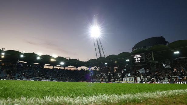 Ein Fußballstadion mit Zuschauern und Flutlicht unter einem Abendhimmel.