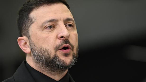 Der ukrainische Präsident Wolodymyr Selenskyj spricht mit ernstem Gesichtsausdruck vor einem dunklen Hintergrund.