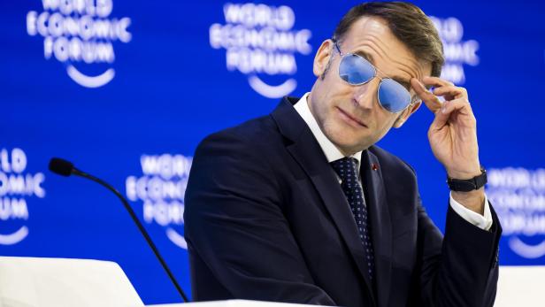 Emmanuel Macron mit Sonnenbrille vor blauem "World Economic Forum"-Hintergrund.