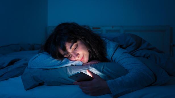 Eine Frau mit Handy im Bett.