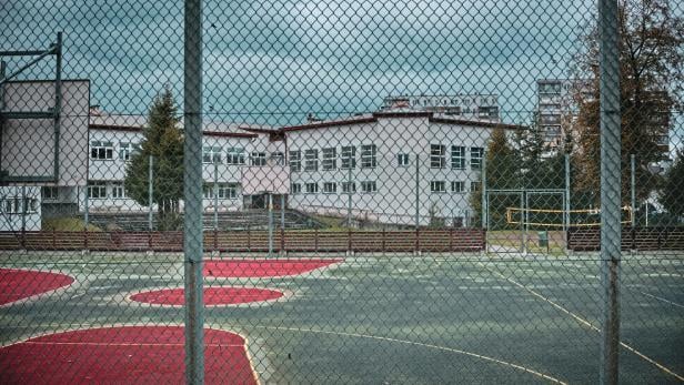 Verlassener Sportplatz mit Basketball- und Fußballfeld, im Hintergrund ein Schulgebäude bei trübem Wetter.