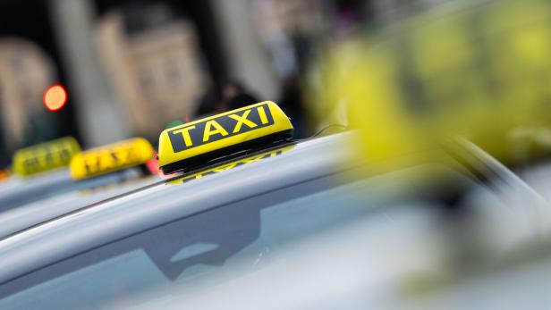 Mehrere Taxis mit gelben Leuchtschildern stehen hintereinander auf einer Straße.