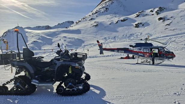 Ein Quad mit Ketten und ein Polizei-Hubschrauber vom Typ OE-BXN stehen vor einer verschneiten Berglandschaft.