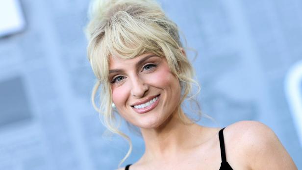 Sängerin Meghan Trainor mit blonden Haaren und Hochsteckfrisur trägt ein schwarzes Oberteil vor unscharfem Hintergrund.