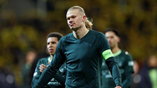 Erling Haaland in Sportkleidung mit "Respect"-Armbinde blickt ernst, Mitspieler im Hintergrund.