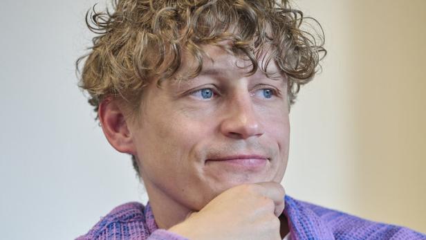Tim Bendzko mit lockigen blonden Haaren trägt ein lila Hemd und blickt nachdenklich zur Seite.