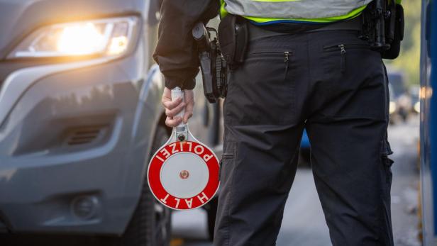 Ein Polizist mit Warnweste hält ein "Halt Polizei"-Schild vor einem Auto.