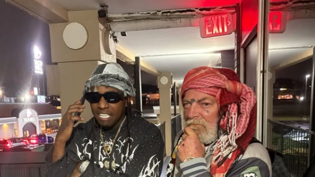 Zwei Männer mit auffälliger Kleidung und Kopftüchern stehen auf einem Balkon bei Nacht.