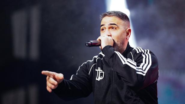 Bushido in Trainingsjacke performt mit Mikrofon und zeigt mit dem Finger.