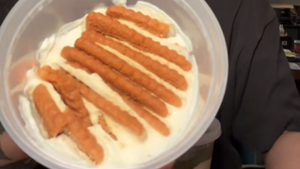 Frau hält Joghurtbecher mit Joghurt und Keksen in die Kamera