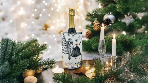 Sektflasche im festlich dekorierten Weinkühler, umgeben von Kerzen und Tannenzweigen.