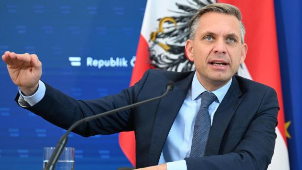 Hattmannsdorfer gestikuliert vor einem Mikrofon, im Hintergrund die österreichische Flagge und ein blaues Banner.