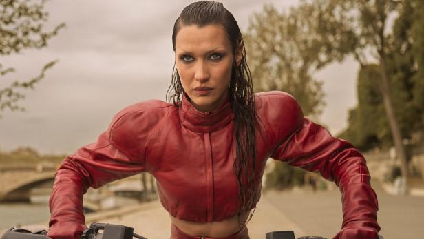 Bella Hadid lenkt in ihrer Serienrolle im roten Lederdress  ein Motorrad