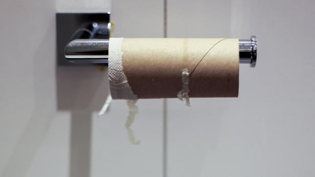 Leere Toilettenpapierrolle an einem Halter vor weiß gefliester Wand.