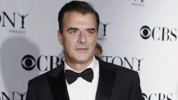 Chris Noth trägt einen schwarzen Smoking mit Fliege vor einem Tony Awards Hintergrund.