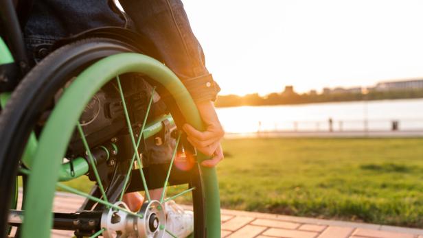 A disabled man is sitting in a wheelchair. He holds his hands on the wheel.