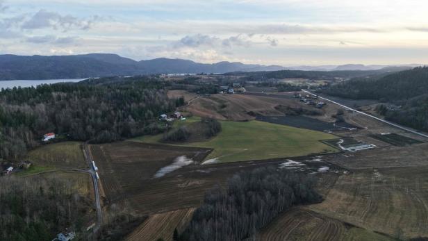 Eine Luftaufnahme des norwegischen Dorfs Ulefoss. Man sieht grüne Felder und Wälder, links im Bild kann man den See und entfernte Hügel entdecken.